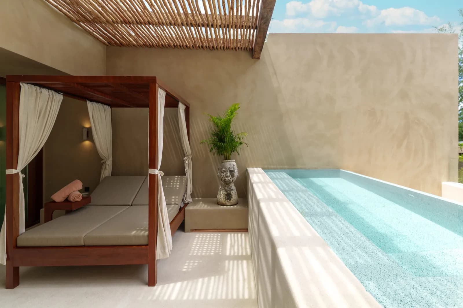 Canopy daybed beside a raised aqua plunge pool under a slatted pergola