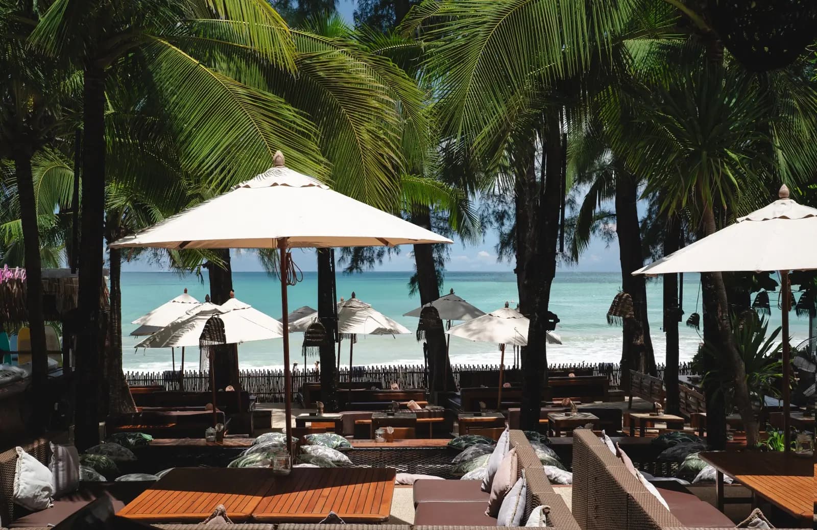 Beach club lounge under palms and white parasols facing the turquoise Andaman Sea