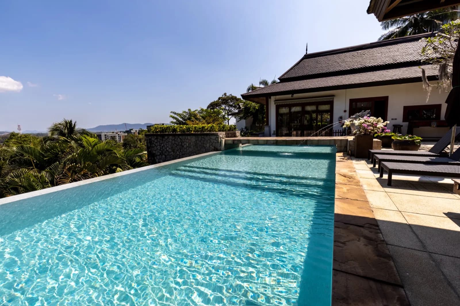 Bright aqua pool with a stone wall beside a Thai-style house