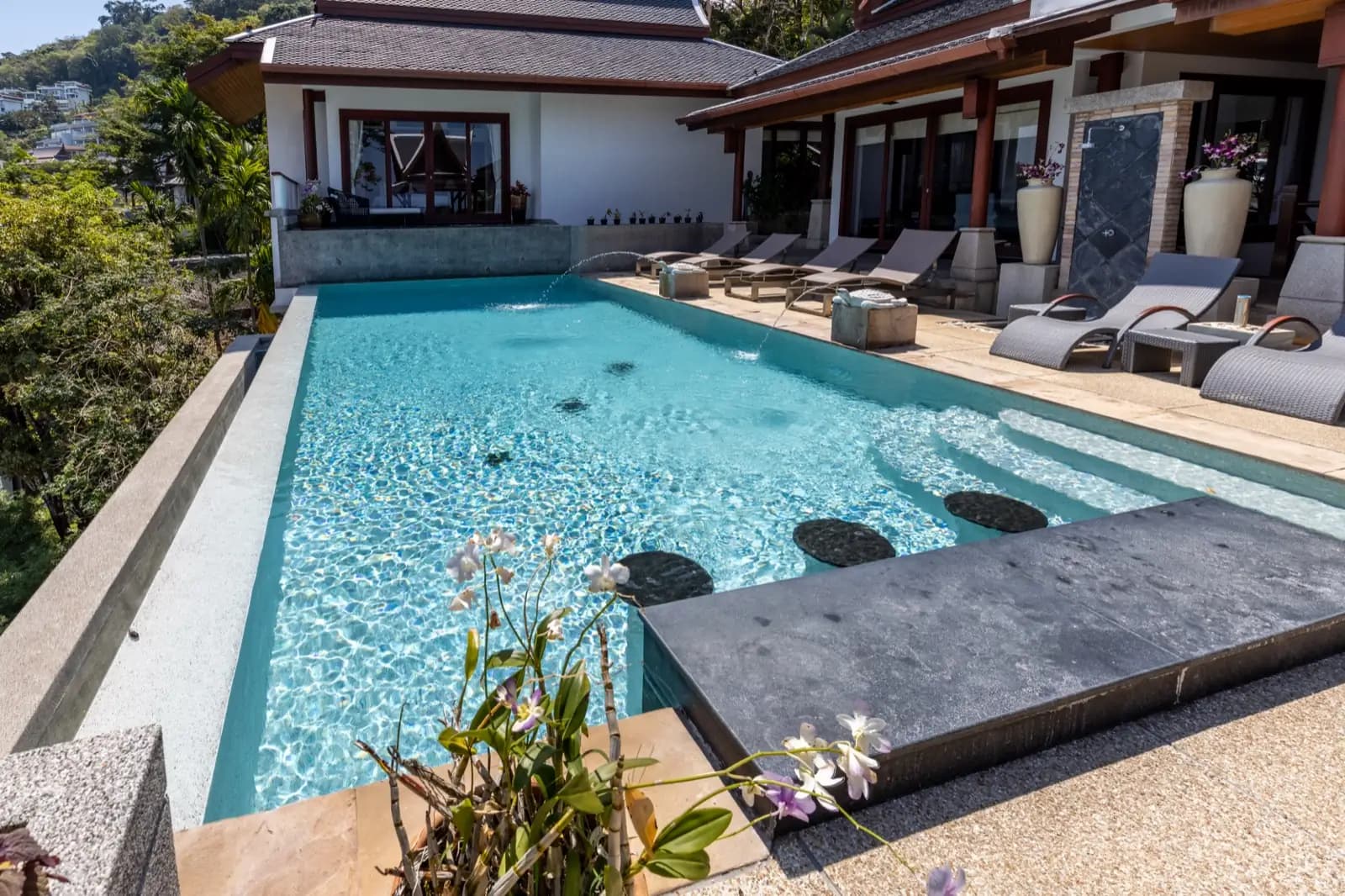 Pool sun-ledge with submerged stools and a slate bar framed by orchids