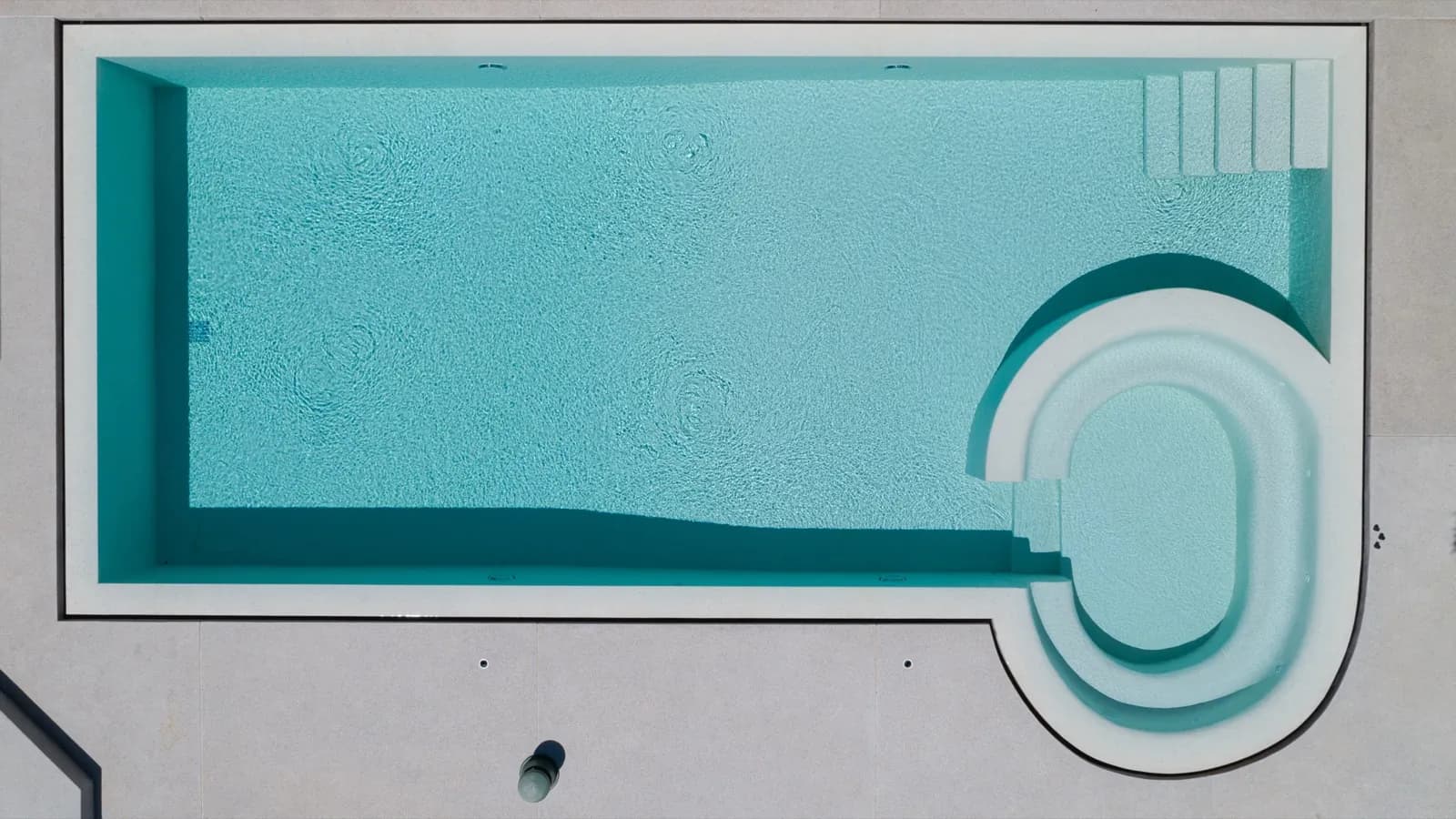 Top-down drone view of a light aqua pool with a rounded lounge and spa end