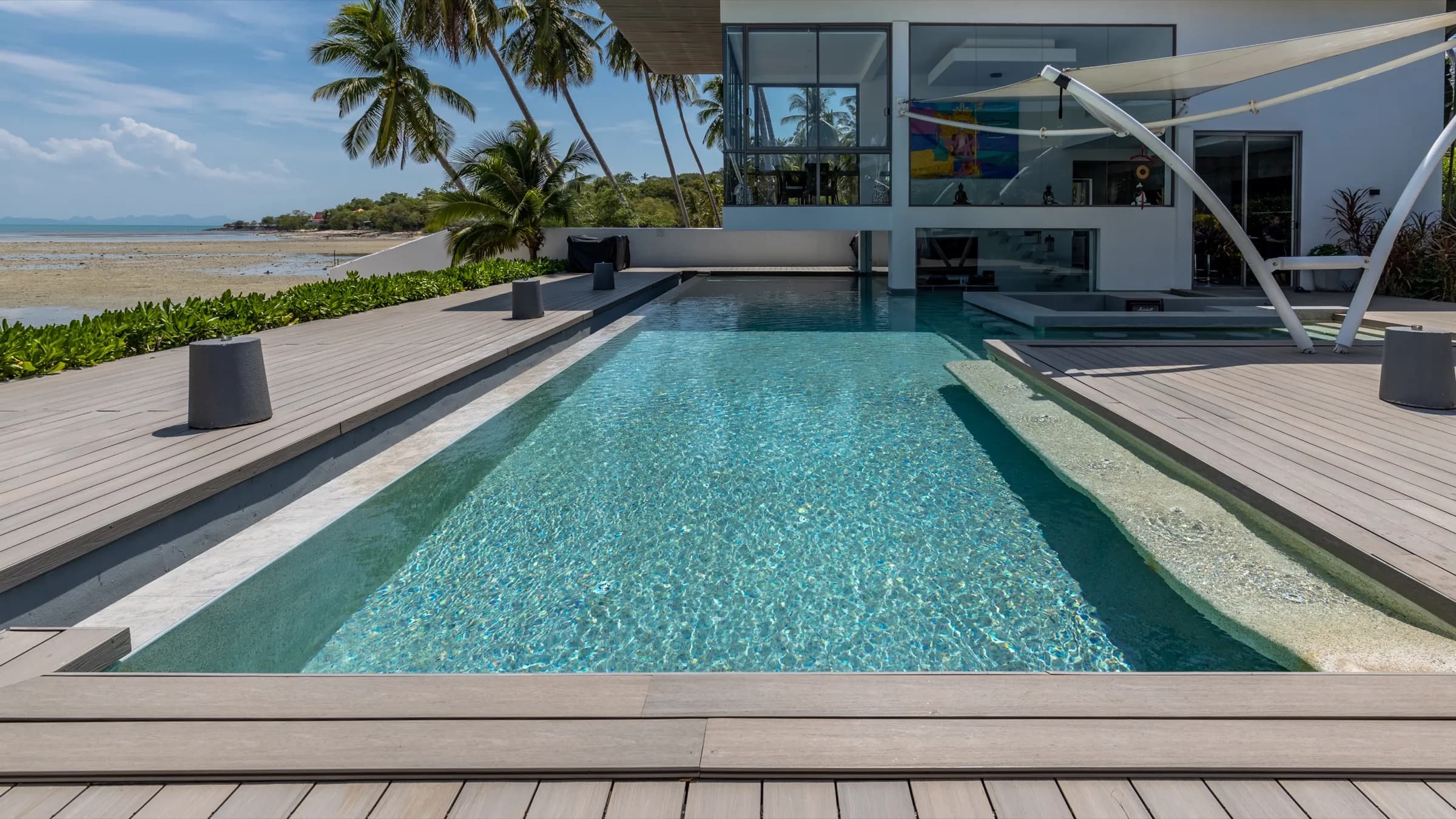 Long clear pool running toward the villa with the beach and palms alongside