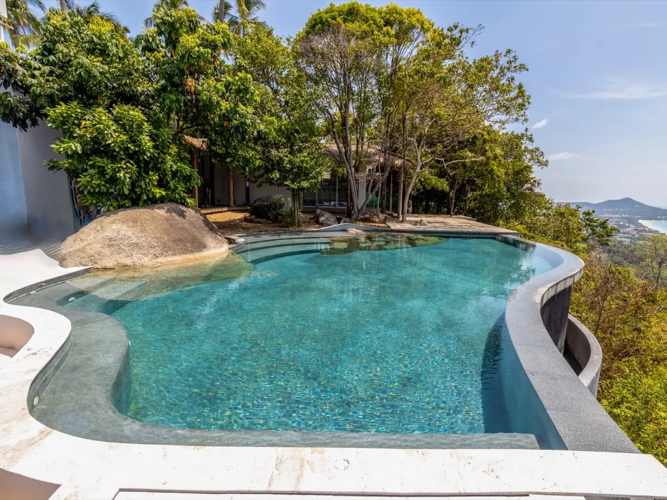 Free-form villa pool with a boulder and wide curving steps under tropical trees