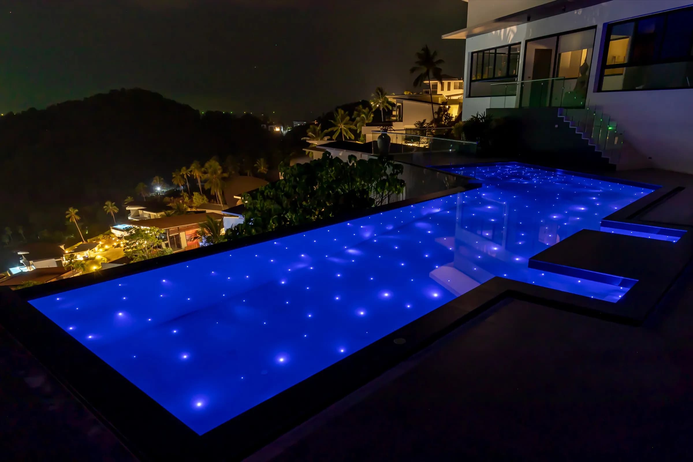 Starlit L-shaped pool at night overlooking the lights of the hillside