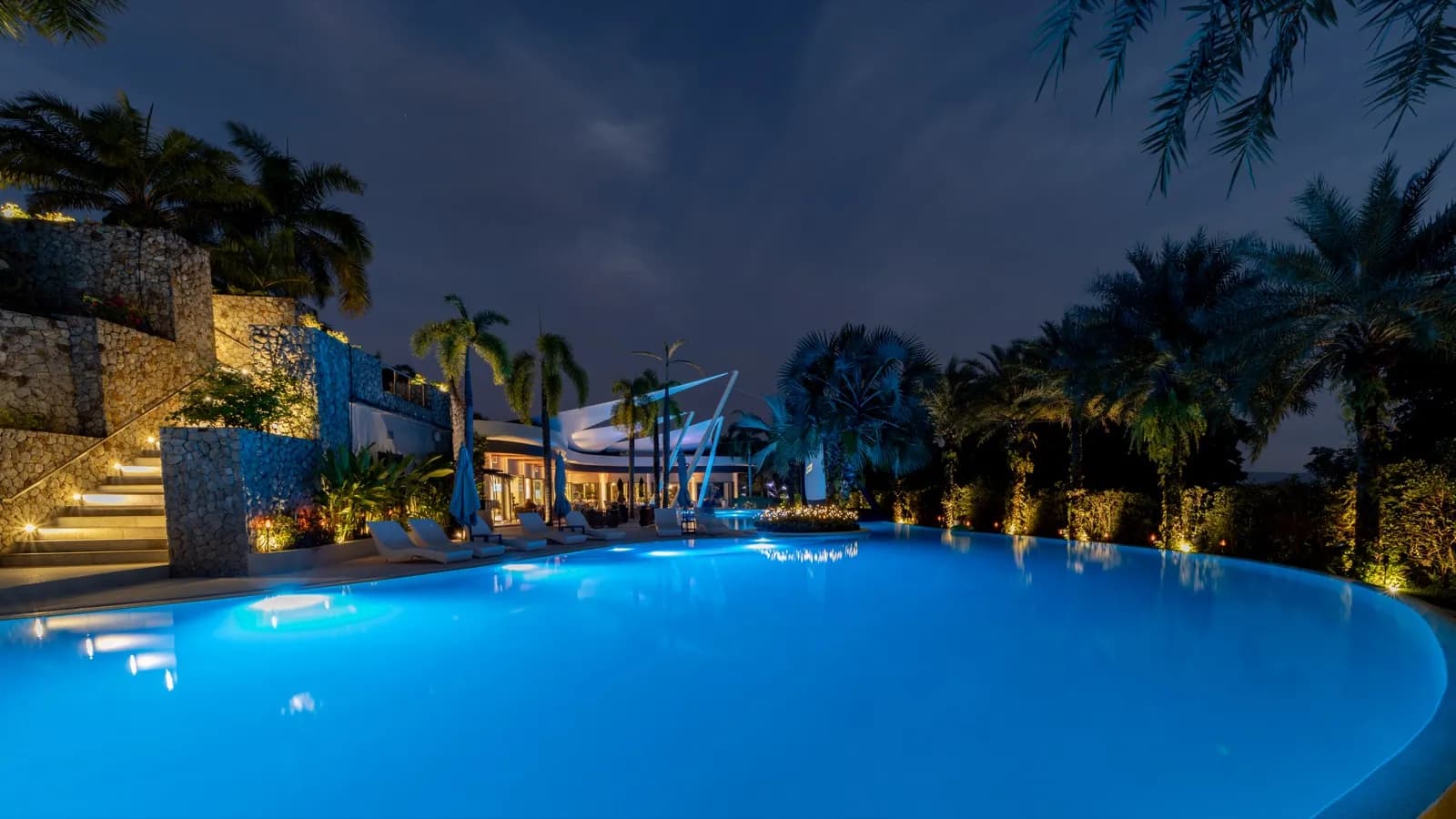 Lagoon pool glowing aqua at dusk with lit terraces and palms