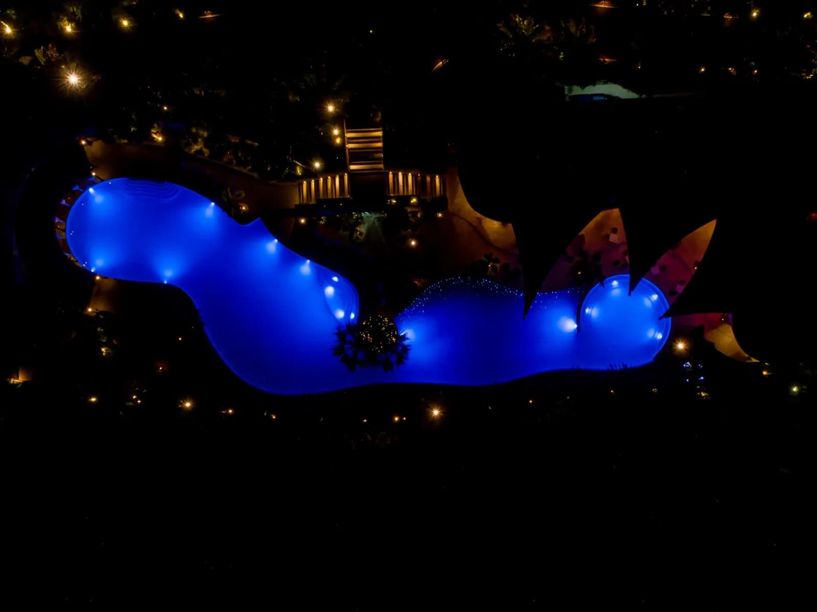 Overhead night drone shot of a winding pool lit electric blue