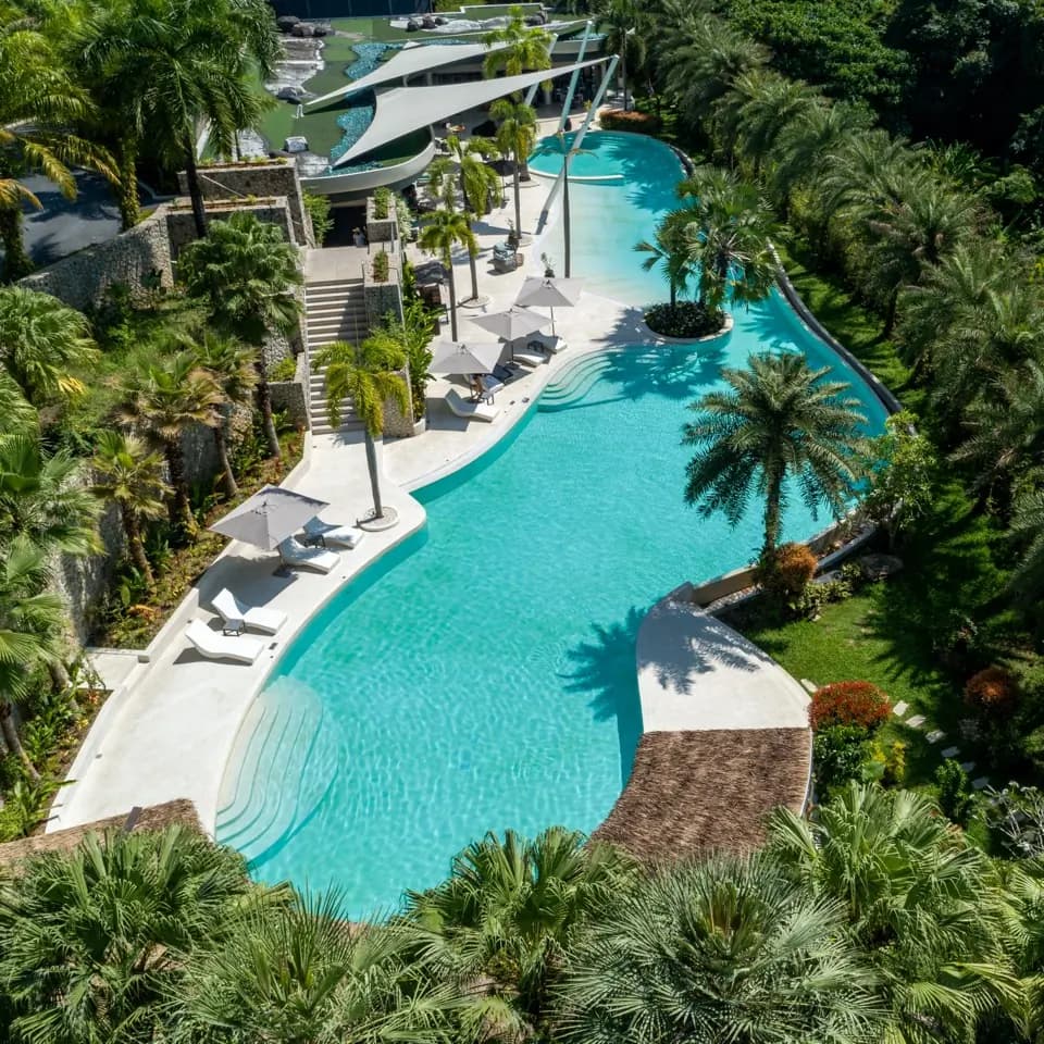 Drone view of a winding aqua lagoon pool with palm islands and white decks