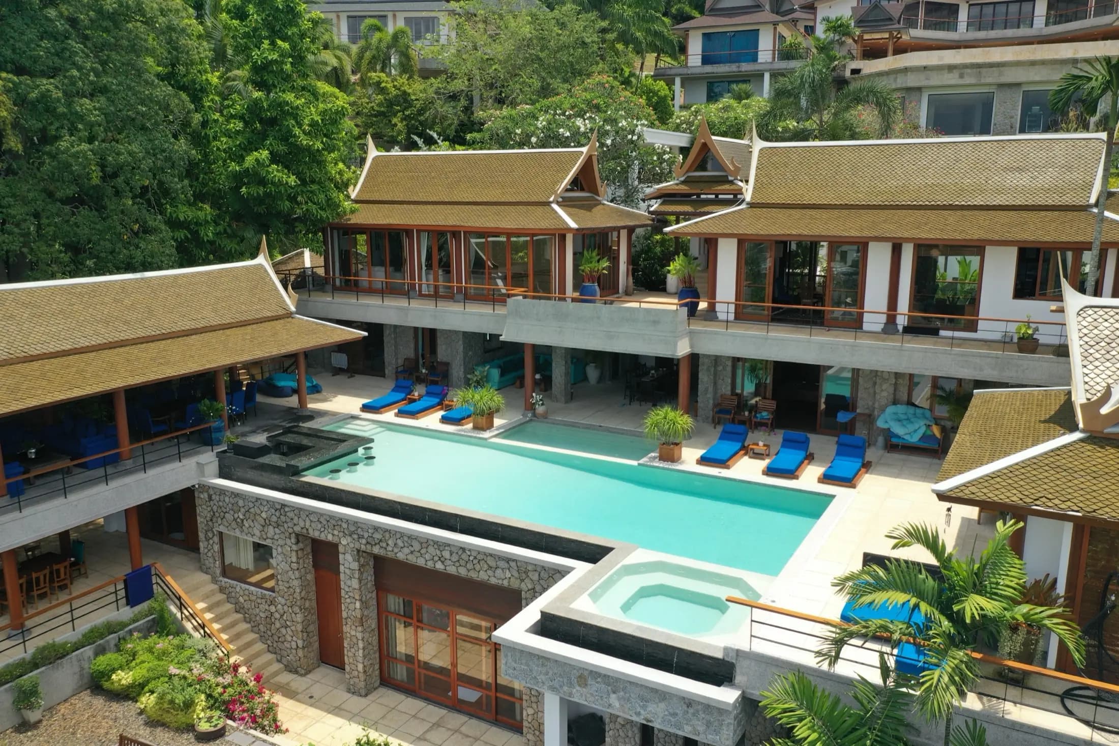 Aerial view of a Thai pavilion villa with a long aqua infinity pool and blue sun loungers