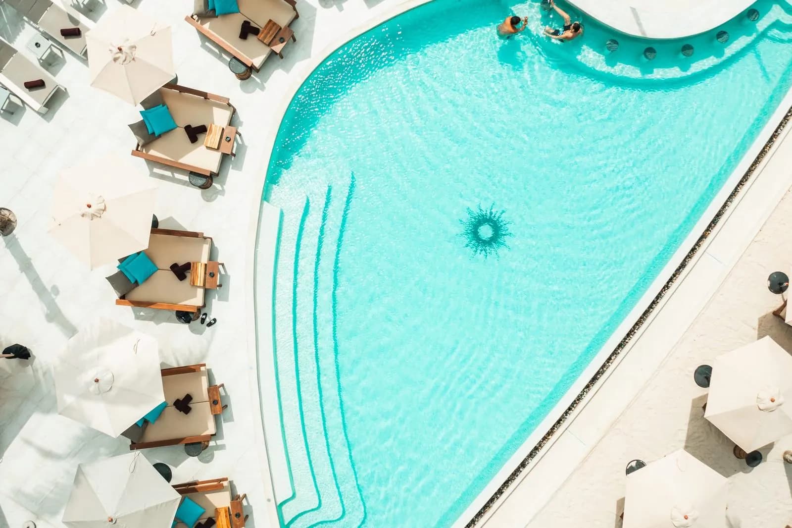 Overhead view of sparkling turquoise water beside daybeds and white parasols