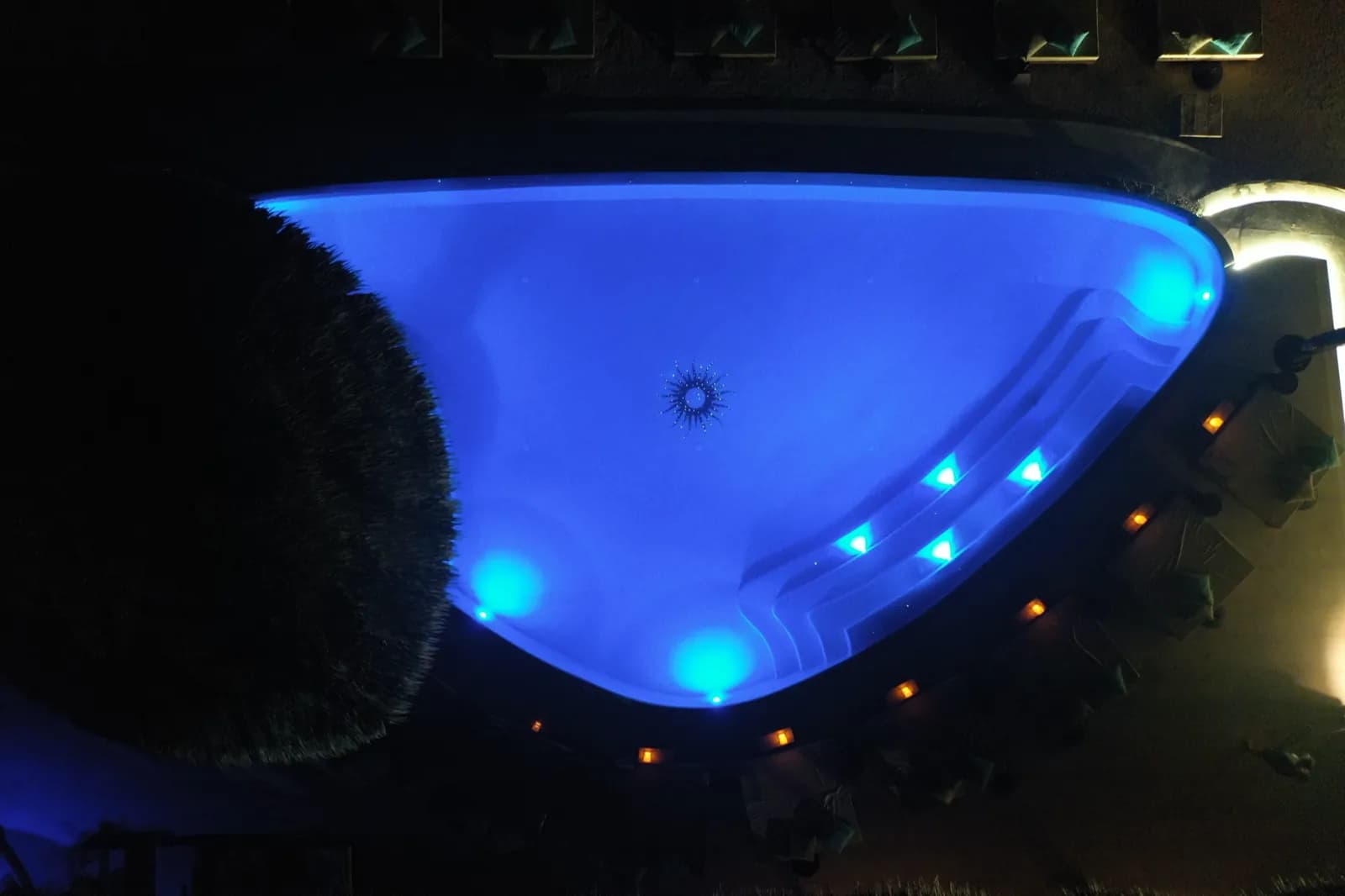 Overhead night view of the blue-lit pool beside the bar