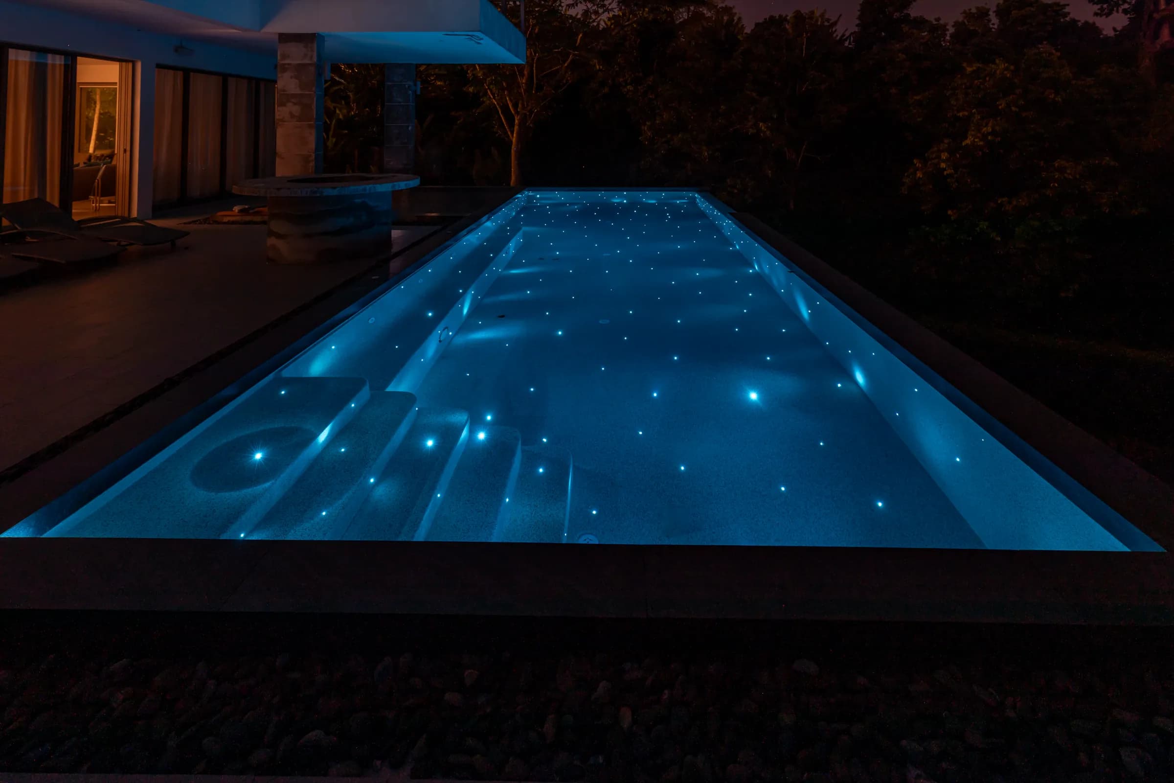 Long lap pool glowing turquoise at night with starlight points and submerged steps