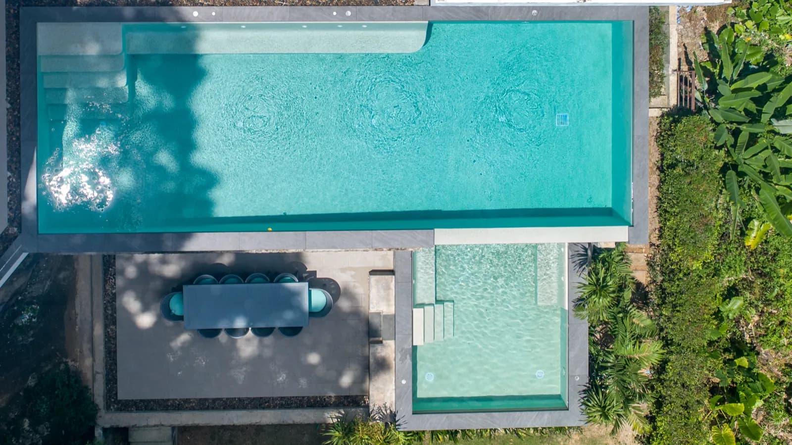 Top-down drone view of a turquoise lap pool, spa and outdoor dining terrace