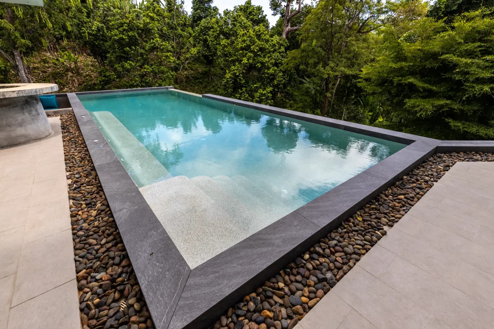 Sharp pool corner framed by dark coping and a river-pebble channel