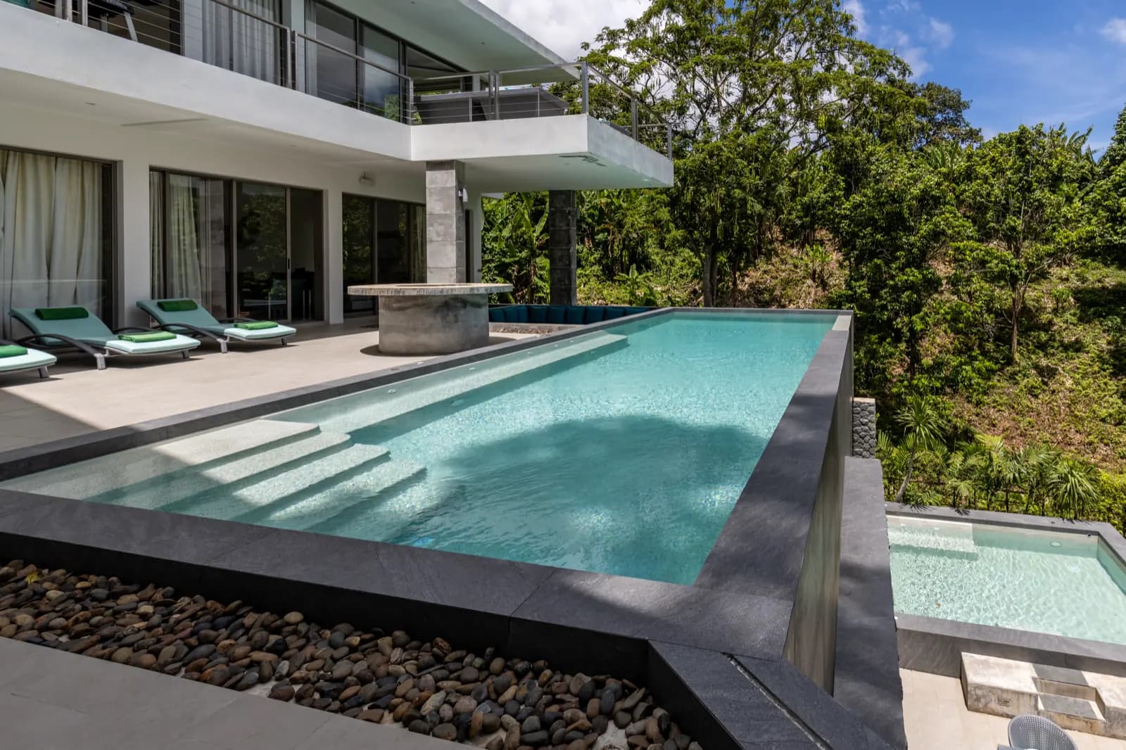 Overflow pool with wide entry steps beside a sun deck and villa terrace