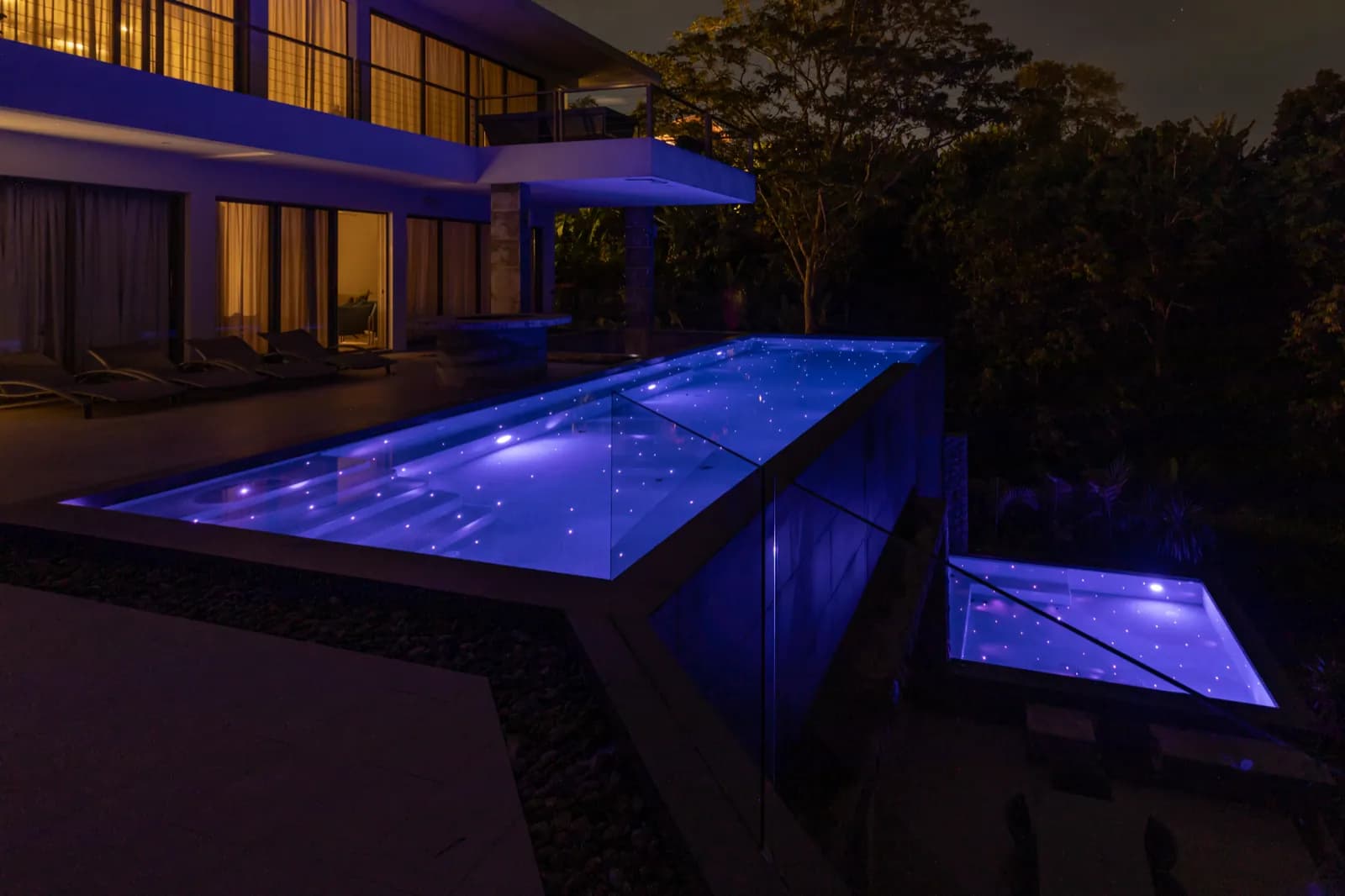 Raised lap pool and spa lit violet after dark beside the villa