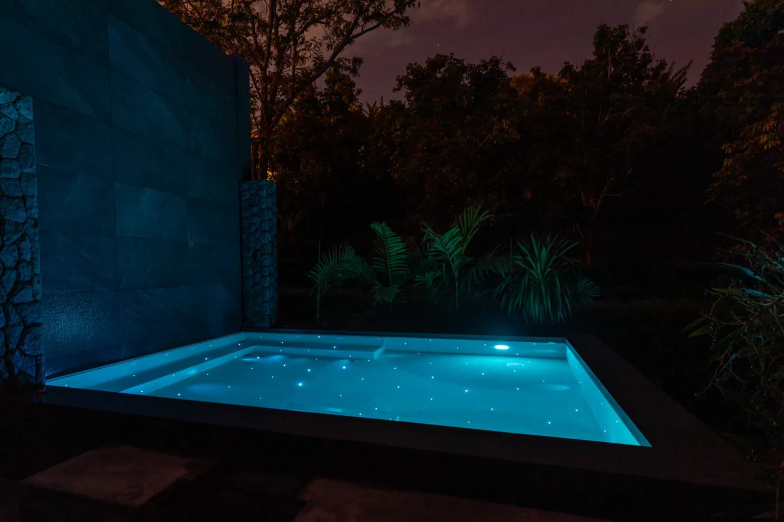 Plunge pool glowing cyan against a stone feature wall at night