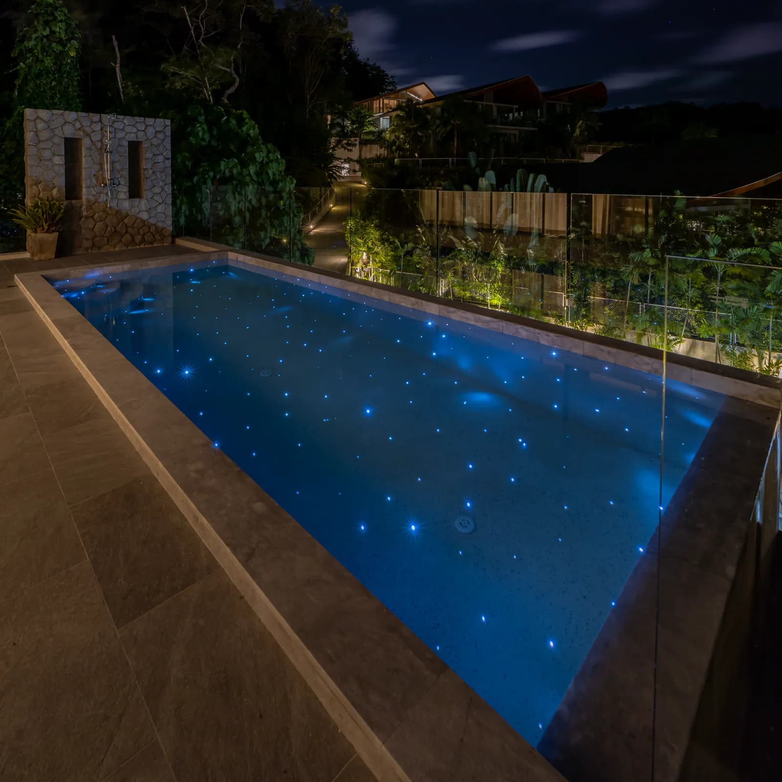 Terrace pool glowing blue with starlight beside lit garden planting