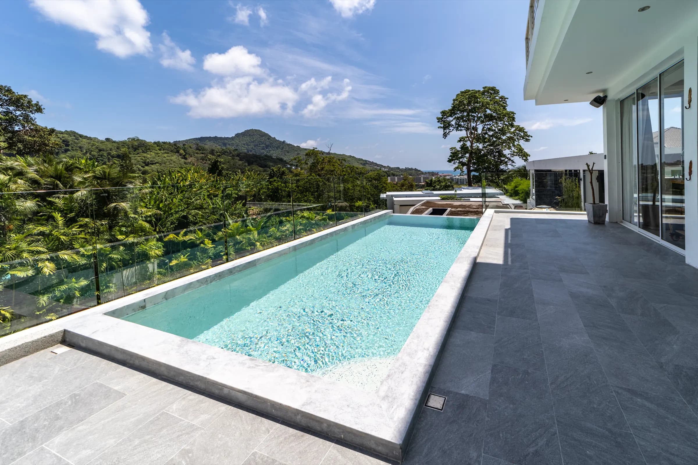 Light aqua lap pool edged in grey marble with a glass balustrade and green mountain views