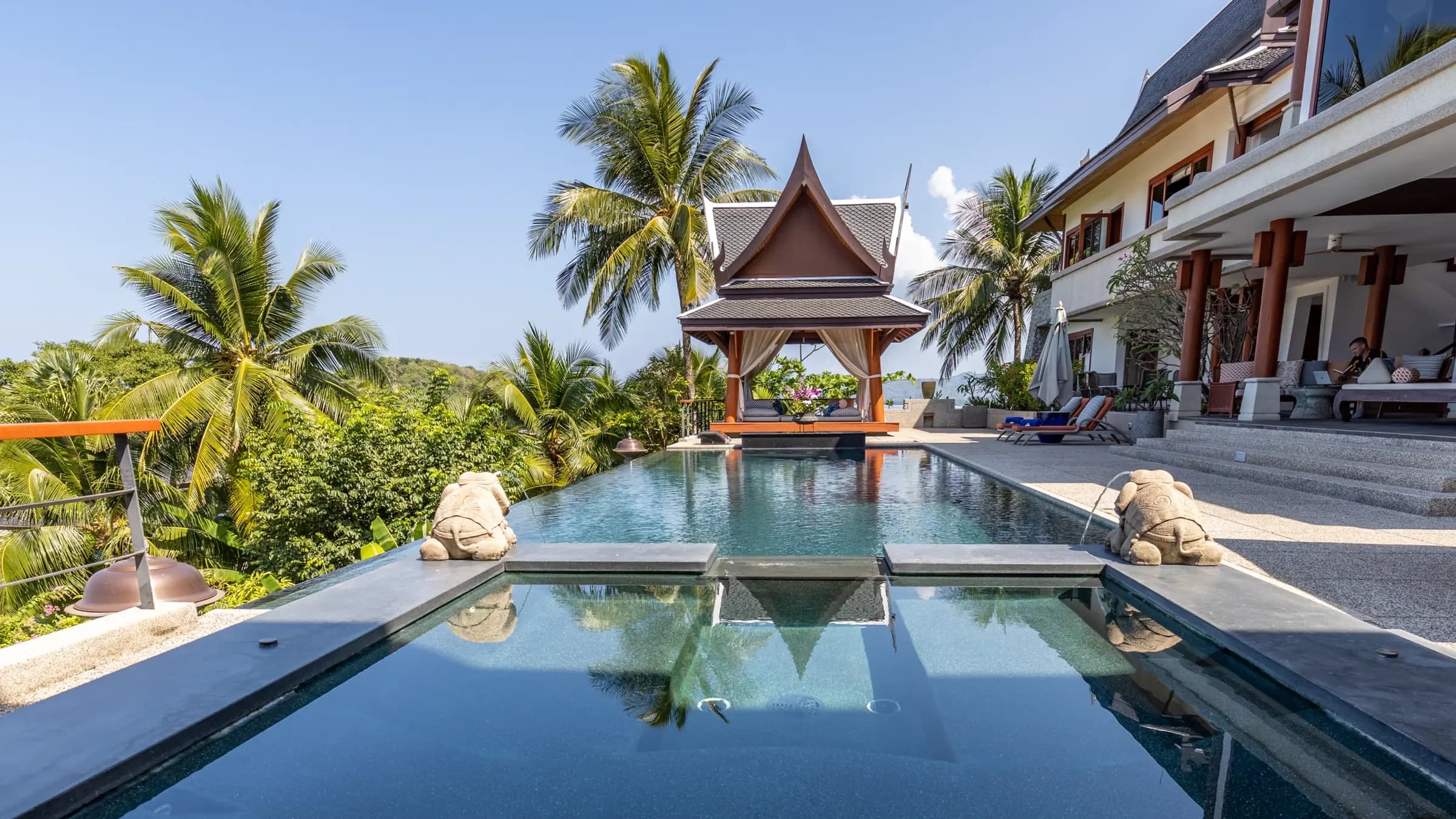 Dark infinity pool with stone elephants leading to a Thai sala above the sea