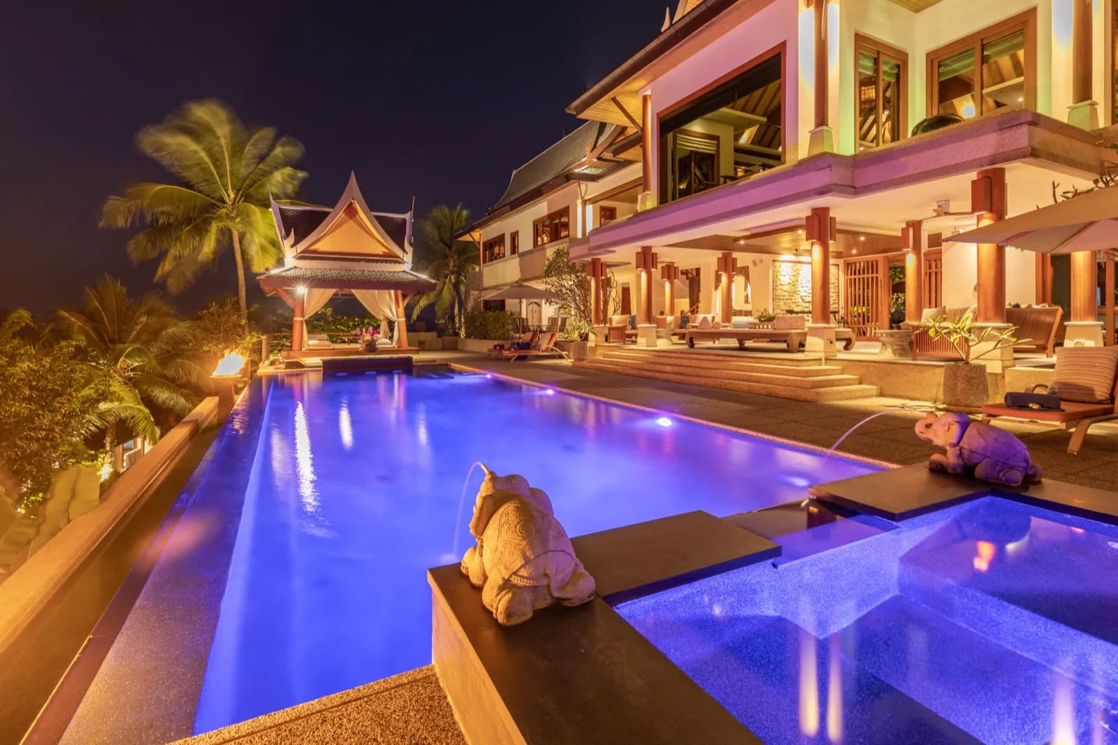 Elephant fountain arcing into a violet-lit pool in front of the illuminated villa