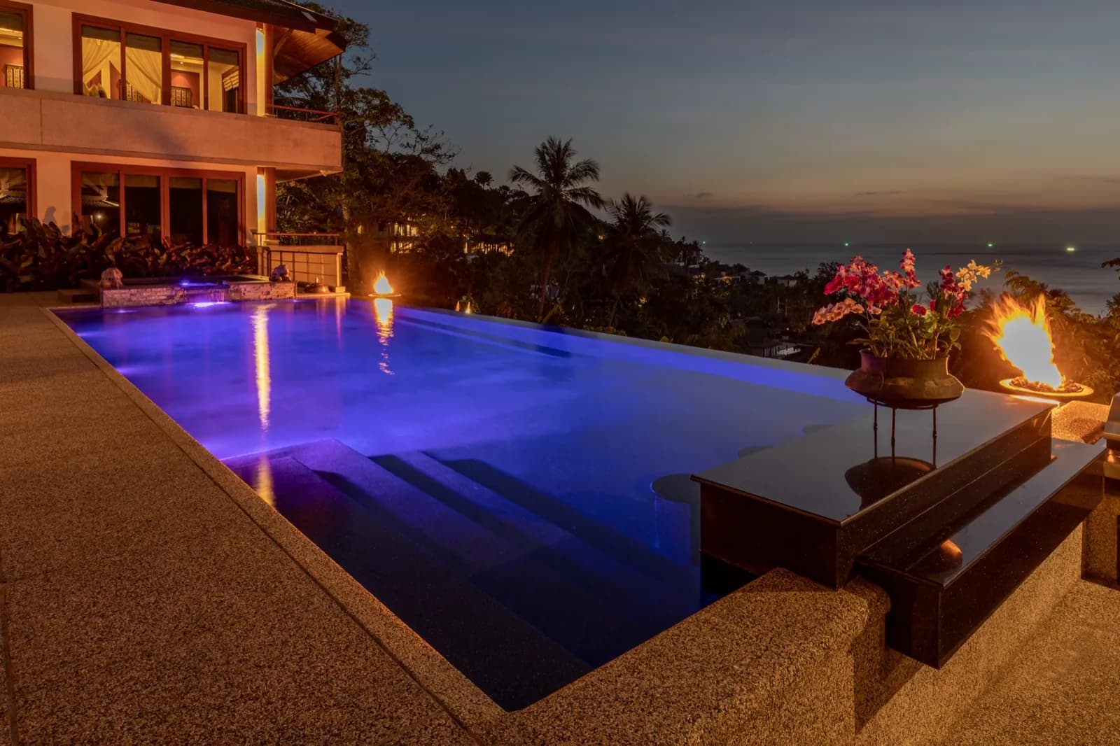Infinity edge glowing blue at dusk beside a fire bowl and orchids