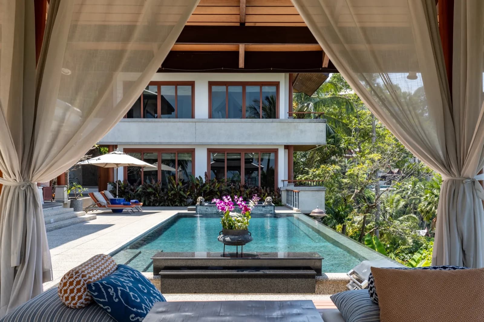 View from a curtained sala across the pool to the villa